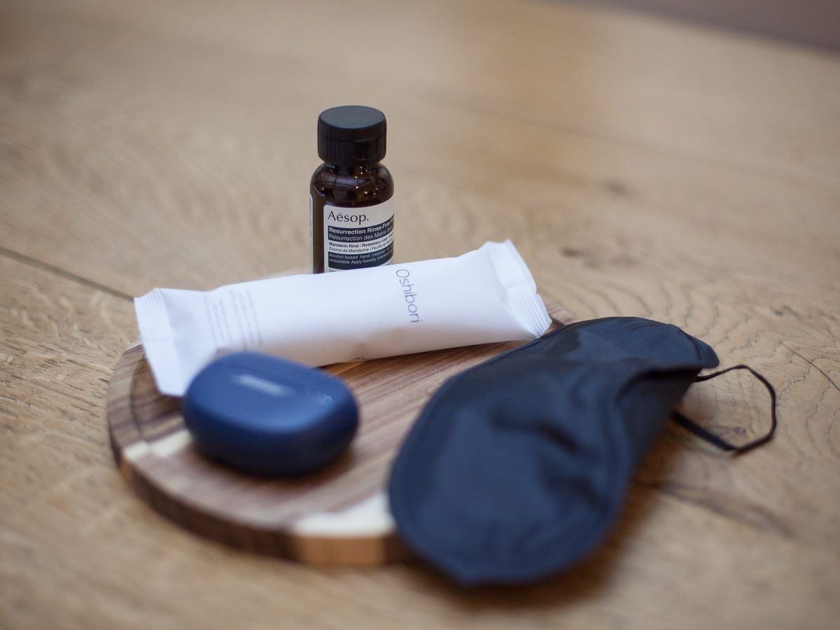 Le nécessaire de la bulle sur un plateau de bois : écouteurs à conduction osseuse, masque de nuit, oshibori et soin des mains