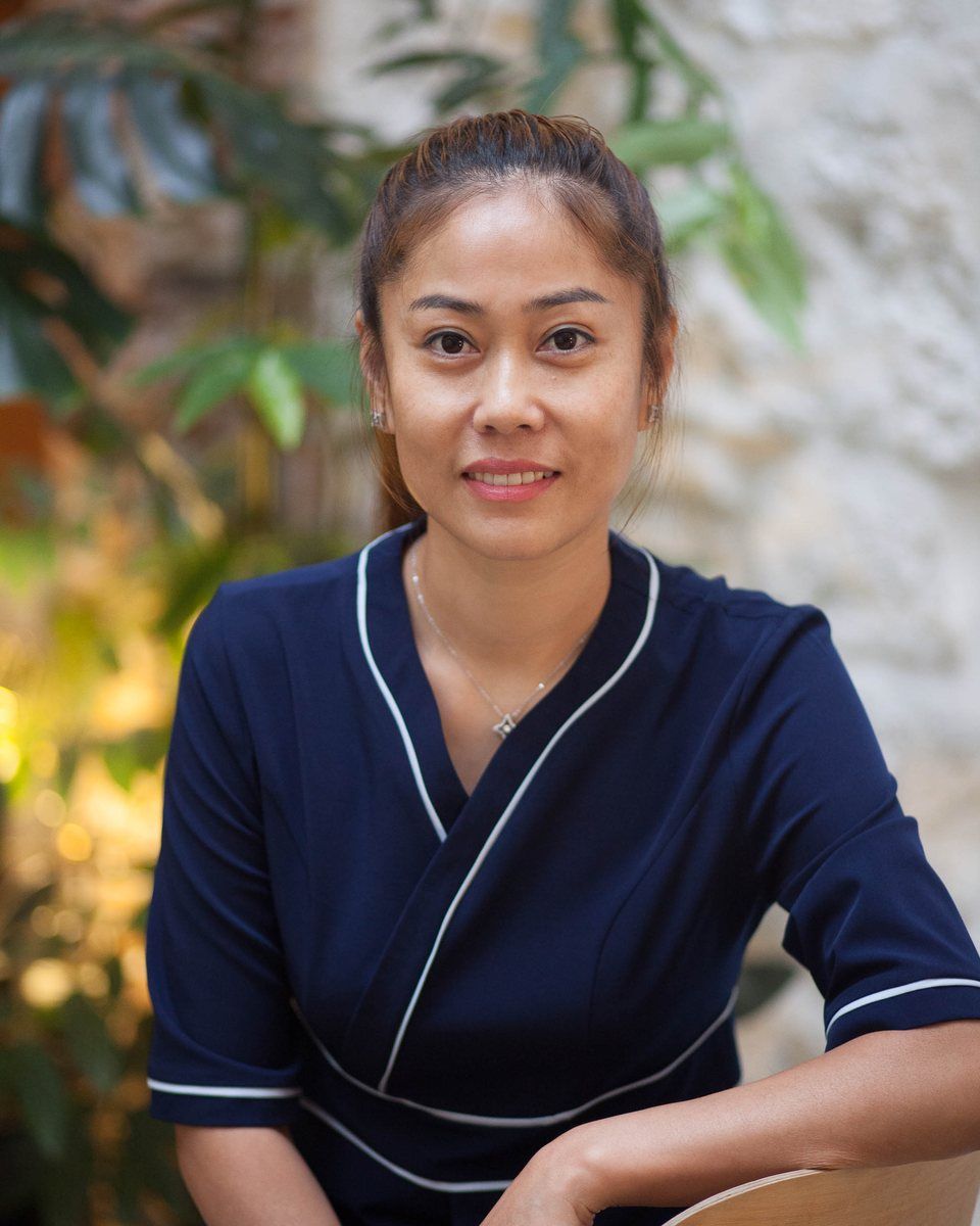 Portrait de Ling, souriante, en tunique bleu nuit, assise devant des plantes